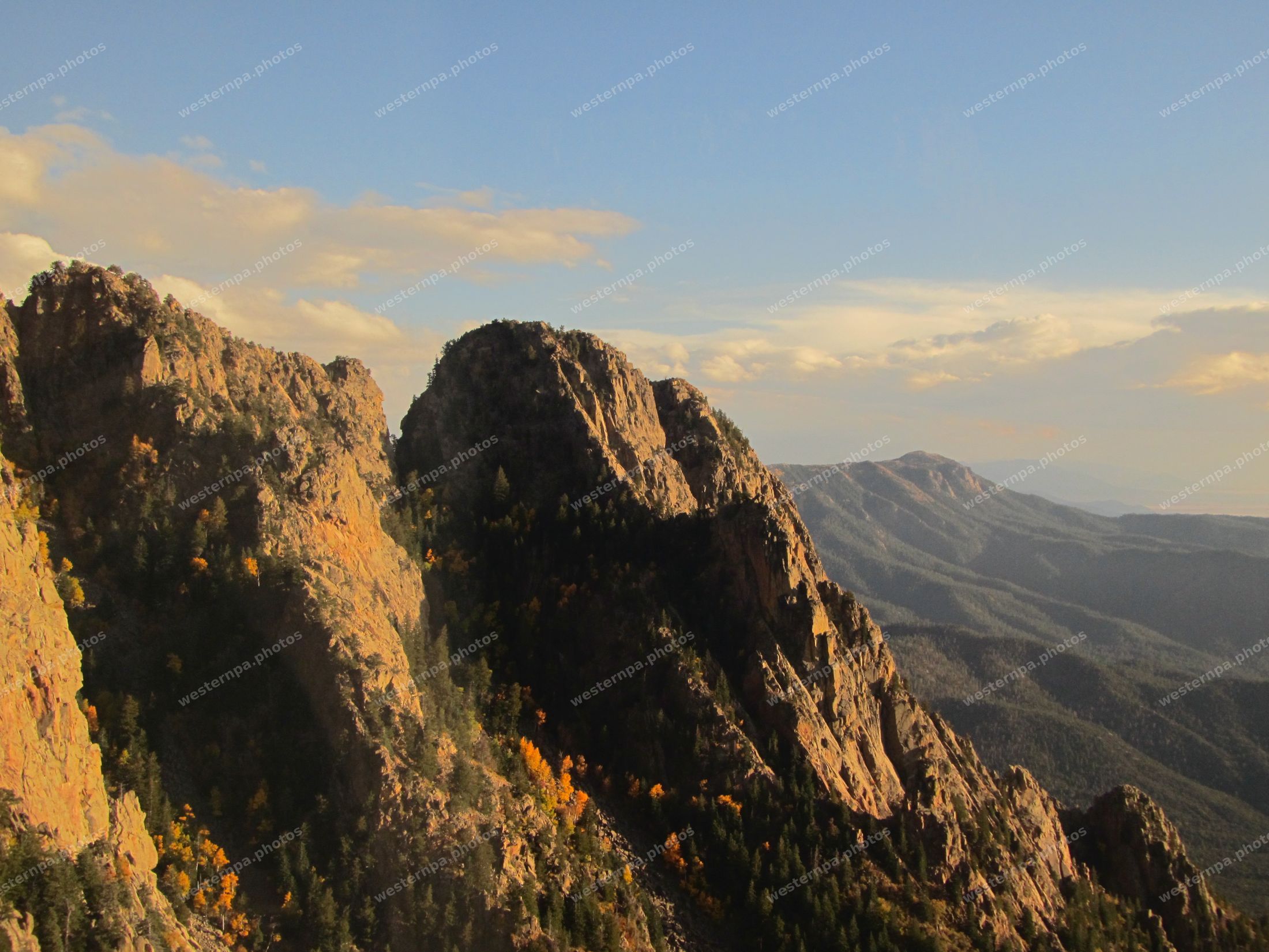 Granite crags with golden autumn aspens and distant blue ridges under evening sky