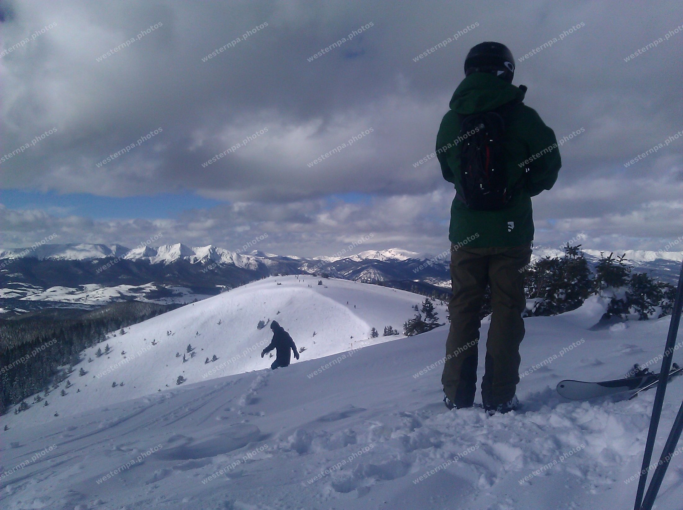 Snowboarder standing in deep snow looking out over a wide winter mountain range