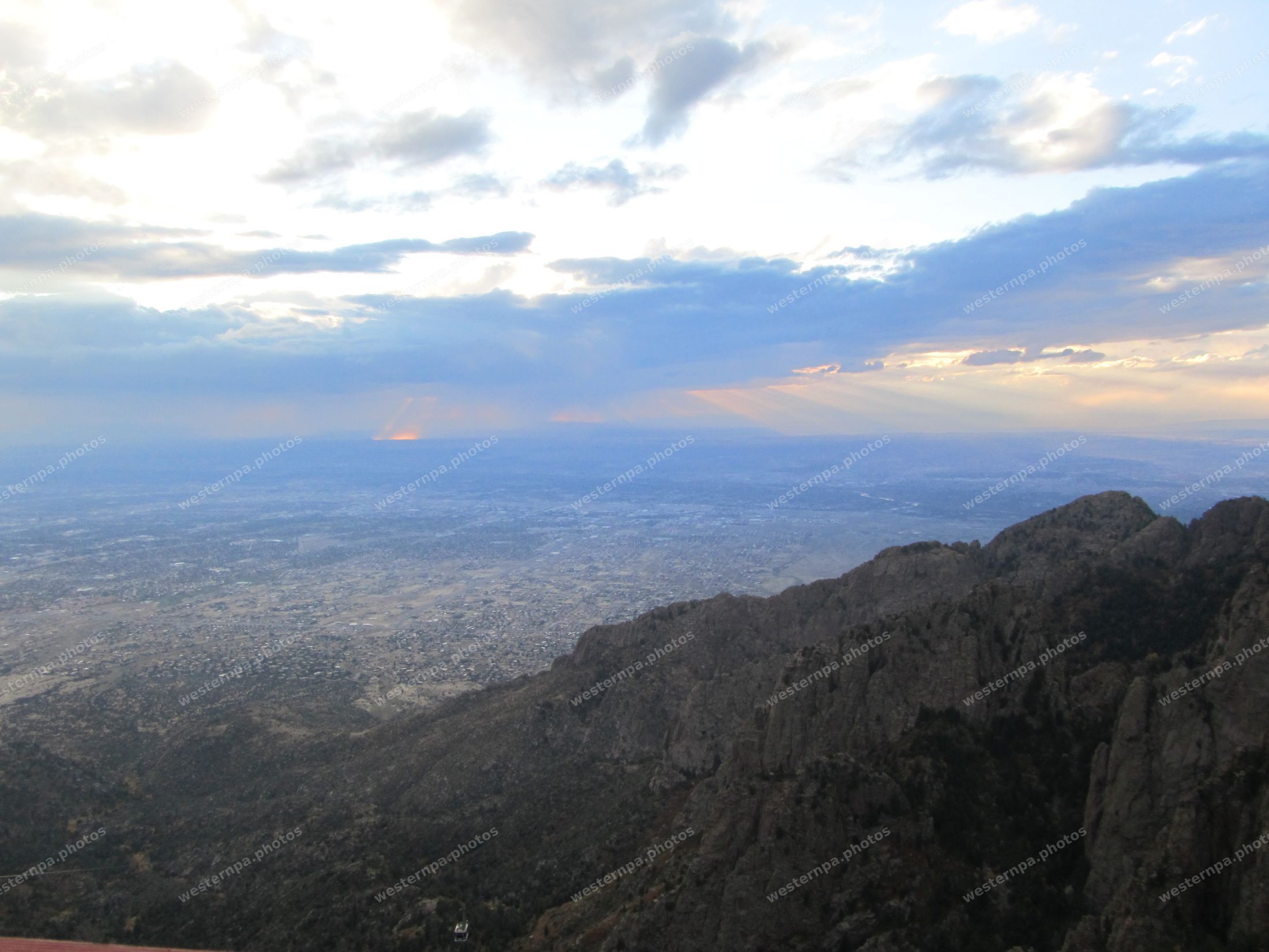 Dusk view from a mountain crest with sunbeams breaking through clouds over a distant city plain