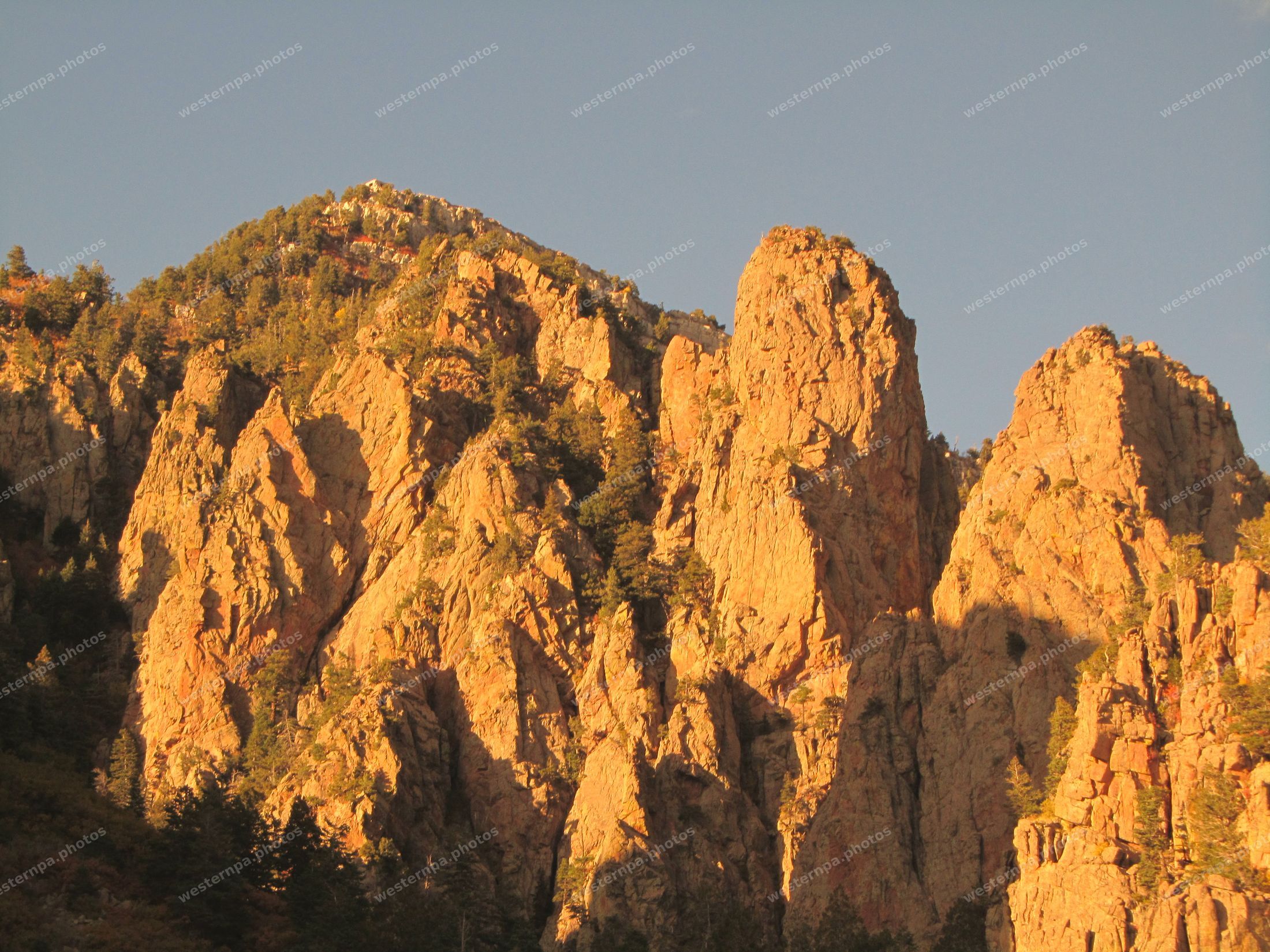 Orange alpenglow on steep granite rock spires with scattered evergreens