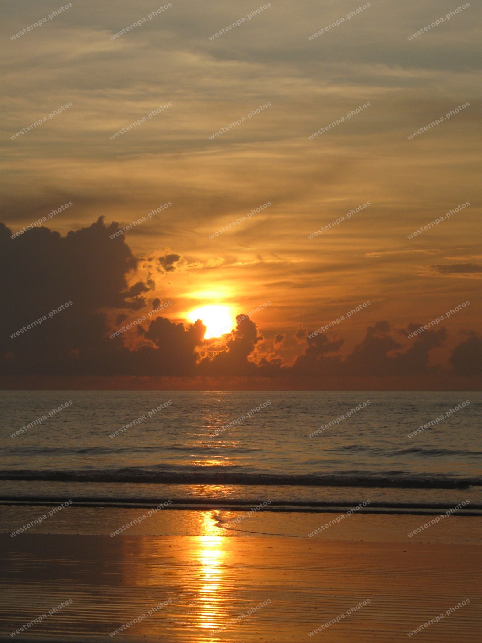 Golden sun low over the ocean reflecting on wet beach sand