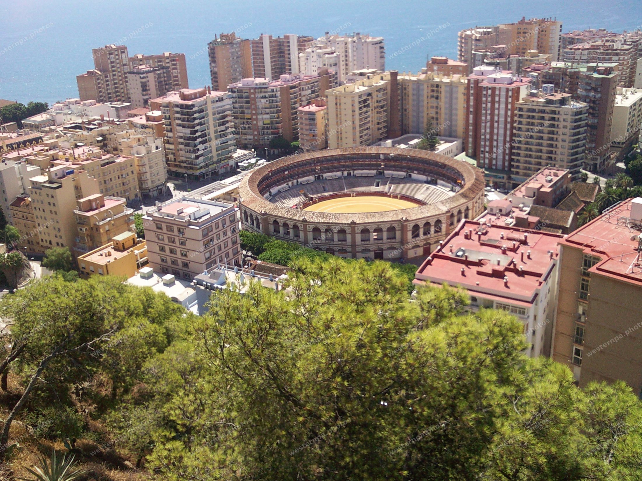Historic round bullring surrounded by city buildings with the Mediterranean Sea behind