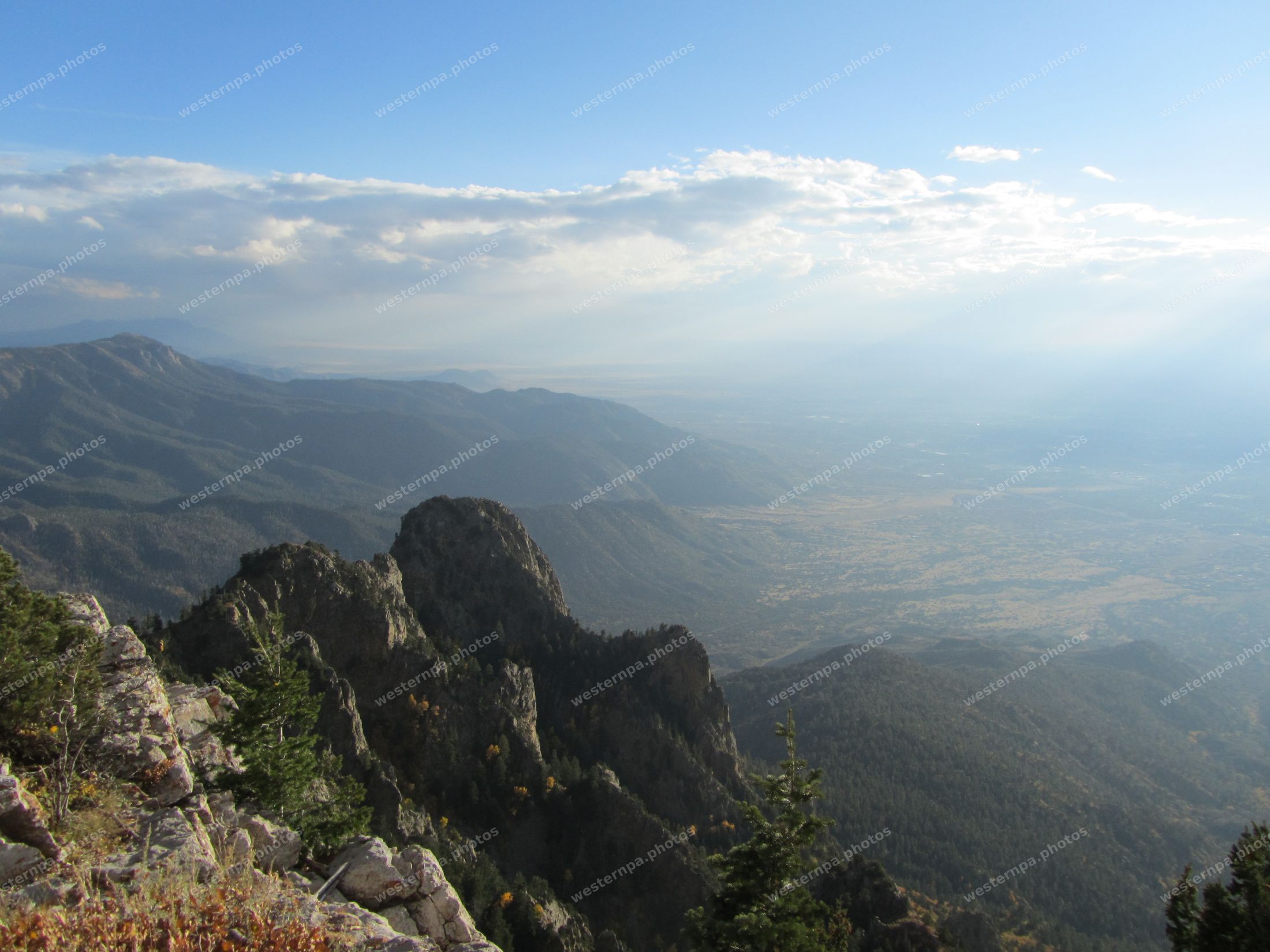 Vast view from a rocky mountain crest over forested ridges and a hazy valley floor