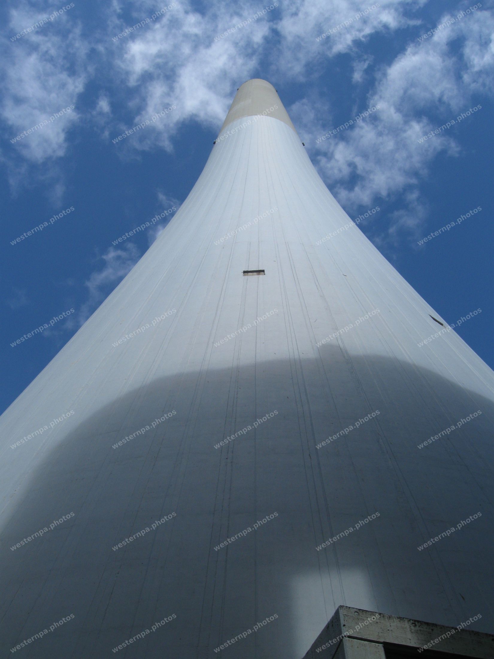 Looking up the sweeping curve of a white concrete tower against blue sky and clouds