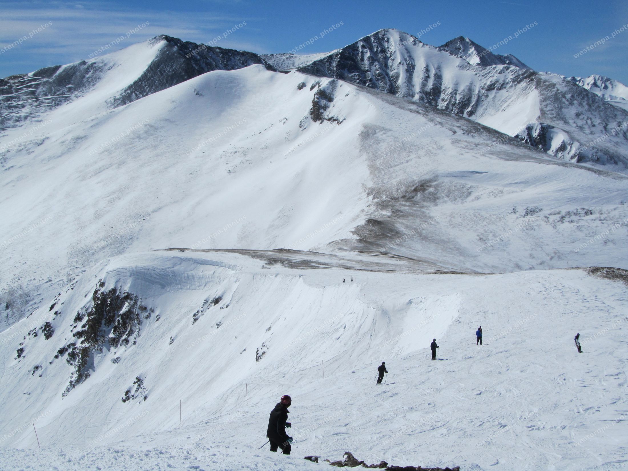 Skiers hiking along a snowy alpine ridgeline beneath high white peaks